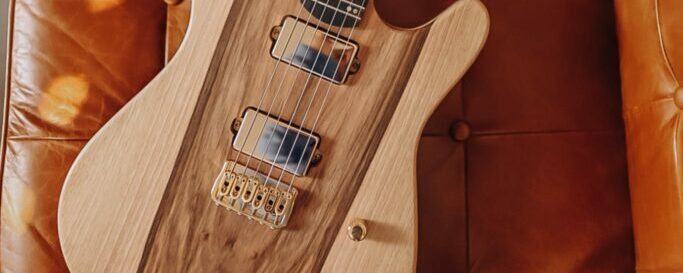 guitare électrique en bois clair posée sur un canapé couleur cognac