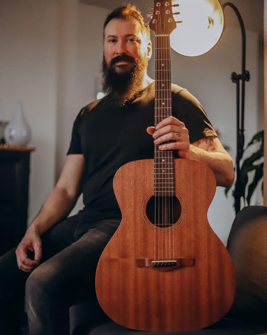 Joey Martin assis sur l'accoudoir d'un fauteuil tenant en main une guitare classique confectionnée par ses soins