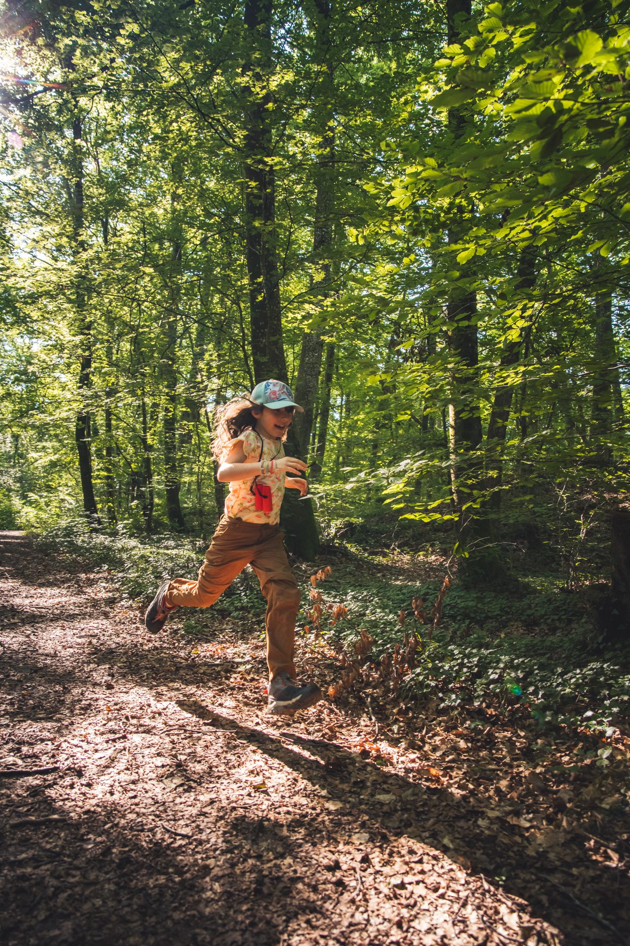 une enfant avec une casquette court dans un rayon de lumière en pleine forêt elle a l'ai heureux